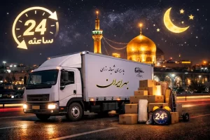 کامیون سفید در شب در مشهد در حال بارچینی بسته‌ها، با نمای گنبد طلایی حرم امام رضا در پس‌زمینه و نماد ۲۴ ساعته، نمایش‌دهنده خدمات باربری شبانه روزی و مطمئن
